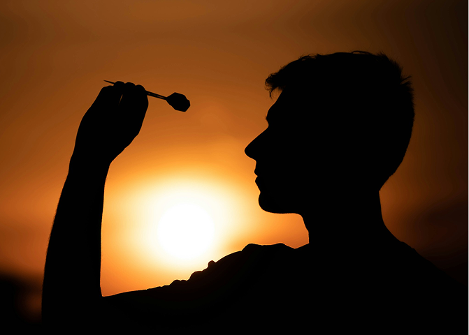 夕焼けをバックに男性がダーツを投げるポーズをしている画像