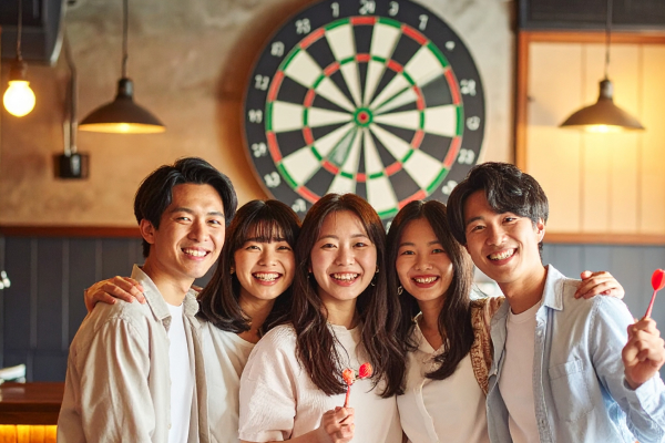 ダーツの的を背に5人で肩を組む男女